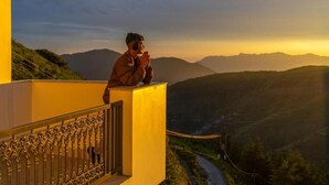 A person sitting on a balcony with a view of a valley and mountains.