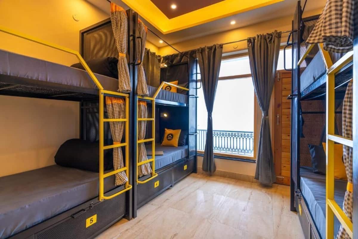 Um dormitório com beliches, uma escada e uma janela com cortinas.
