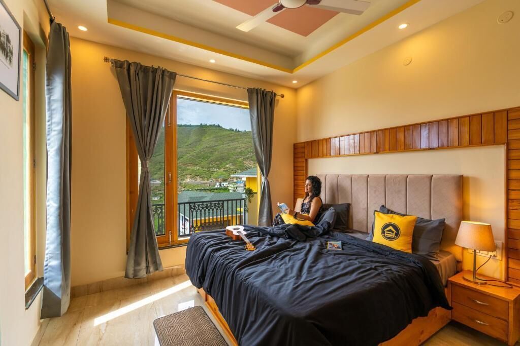 Une chambre à coucher avec un grand lit, une table de chevet, une fenêtre avec des rideaux et une vue sur un paysage verdoyant.