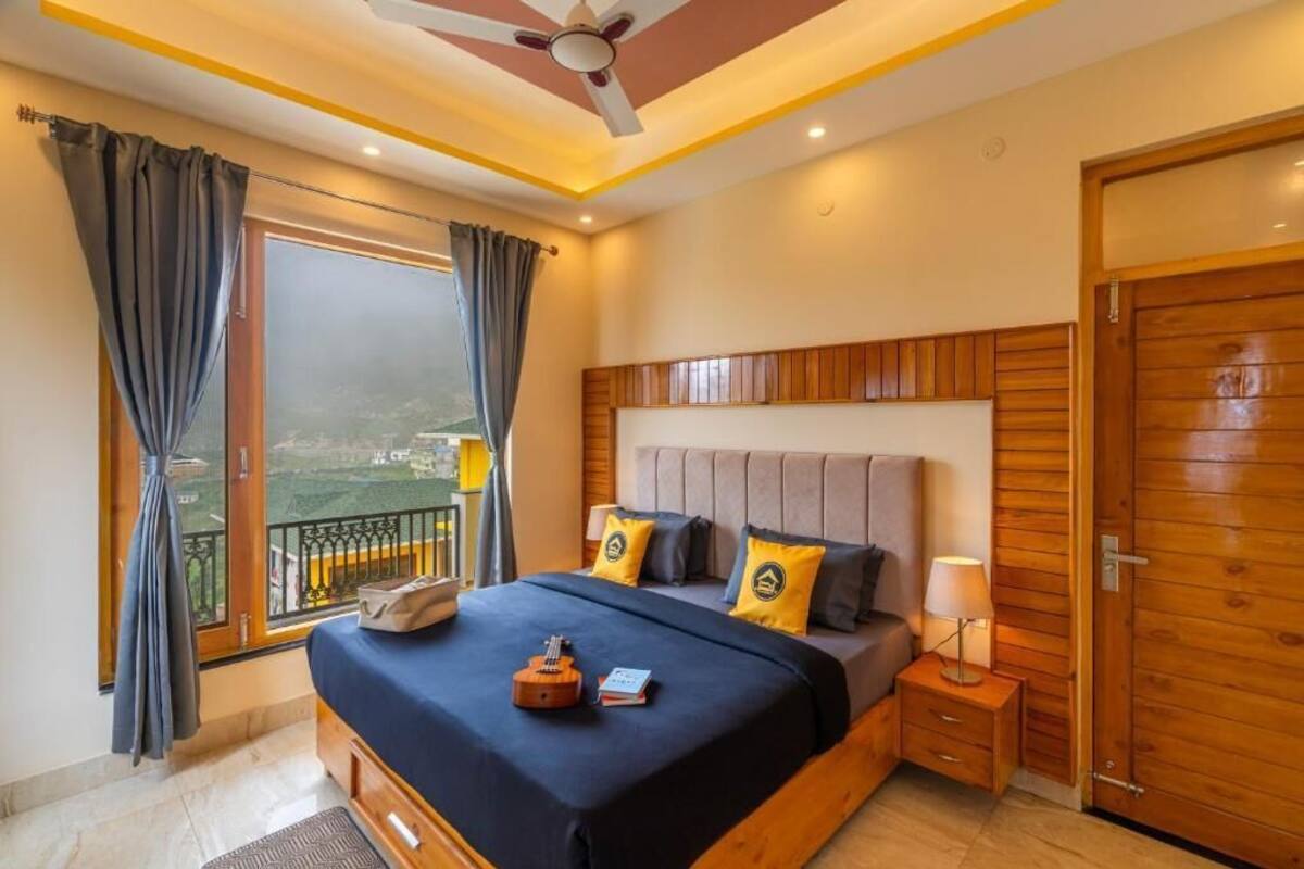 Quarto com cama grande, mesa de cabeceira, luminária, ventilador de teto e vista para o exterior.