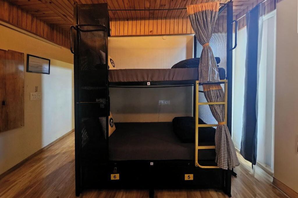 Una cama litera con escalera y un estante pequeño, un calentador y una ventana con cortinas.