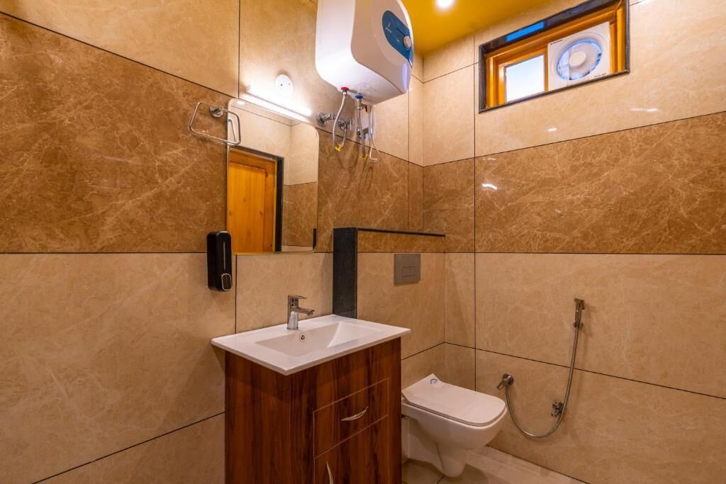 A bathroom with a marble wall, a wooden vanity, a white sink, a toilet, and a shower.