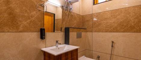 A bathroom with a marble wall, a wooden vanity, a white sink, a toilet, and a shower.