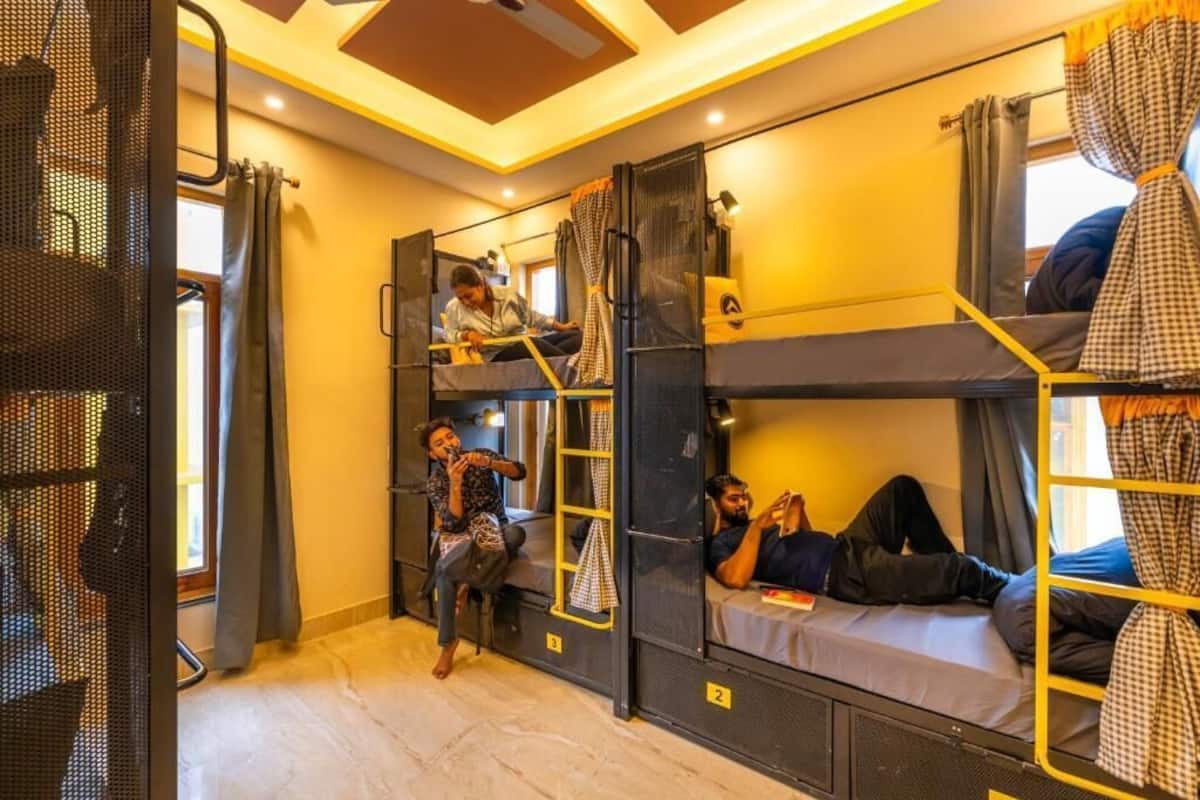 Quarto tipo dormitório com beliches, escada e janela com cortinas.
