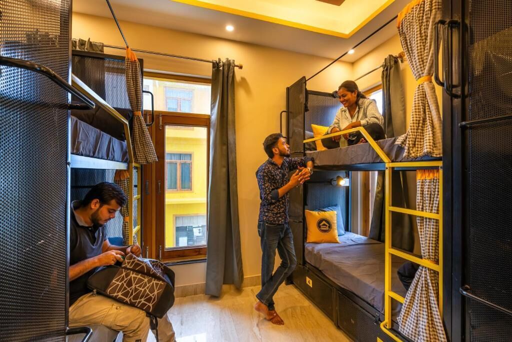 A compact hostel room with bunk beds, a window with curtains, and a small table.