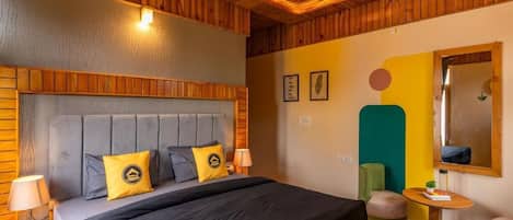 A bedroom with a wooden ceiling, a bed with a grey headboard, and a small table with a lamp.