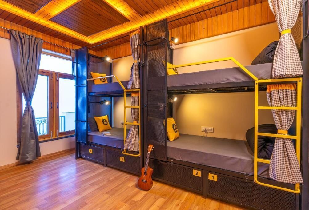 Habitación con literas, una guitarra, pisos de madera y una ventana con cortinas.