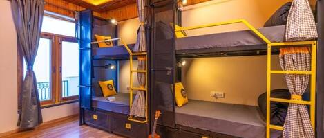 Habitación con literas, una guitarra, pisos de madera y una ventana con cortinas.