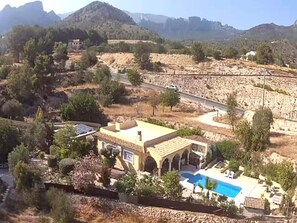 A Mediterranean-style villa with a swimming pool, surrounded by dry vegetation and mountains.