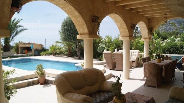 A covered outdoor area with a pool, seating, and potted plants.