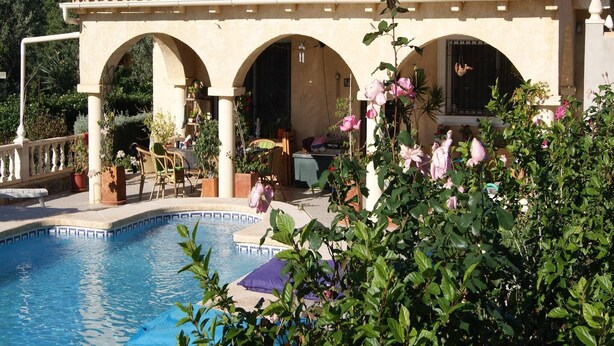 A poolside area with a tiled roof, arches, and outdoor furniture.