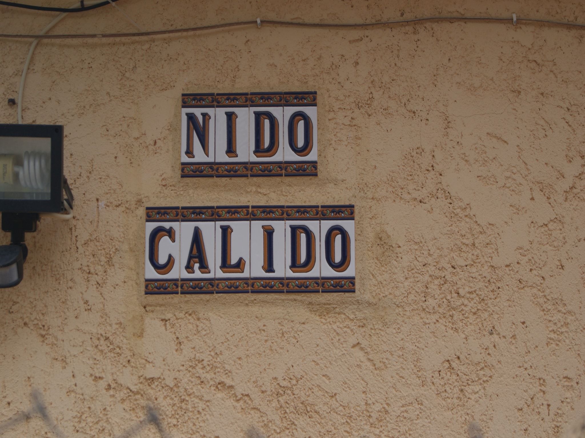 Dos letreros sobre una pared con textura, uno dice 'NIDO' y el otro 'CALIDO'.