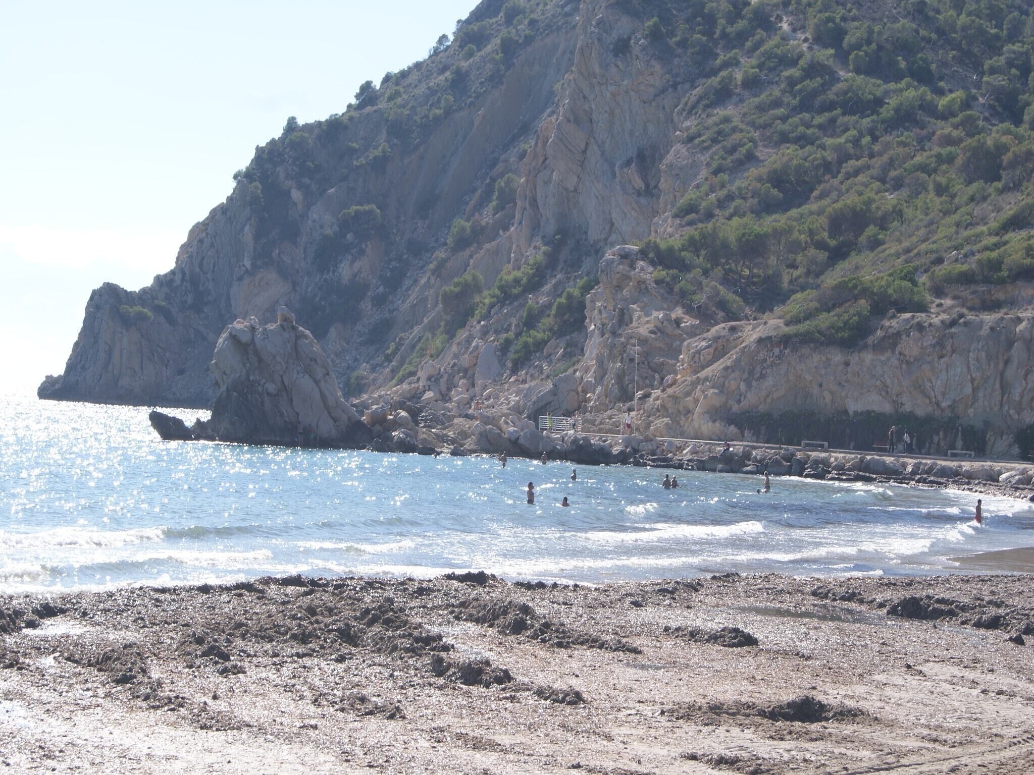 A rocky beach with a rocky cliff in the background.