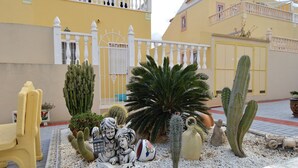A courtyard with a white gate, yellow walls, and various cacti and sculptures.