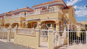 A multi-story building with balconies, a gated entrance, and a clear sky.