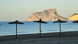 Une plage avec des parasols en chaume et une montagne rocheuse en arrière-plan.