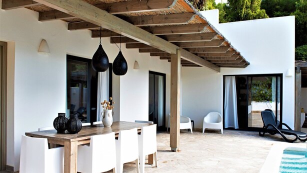 Une terrasse extérieure avec une table et des chaises en bois, un luminaire suspendu et une piscine.