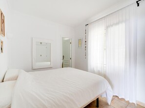 Ein Schlafzimmer mit einem großen Bett, einer Tür, einem Spiegel und einem Fenster mit transparenten Vorhängen.