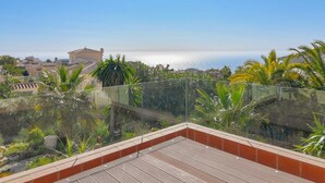 Una terraza en la azotea con vistas al mar, rodeada de vegetación y palmeras.
