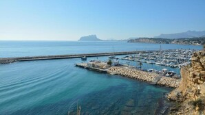 A marina with boats docked, a rocky coastline, and a distant mountain.