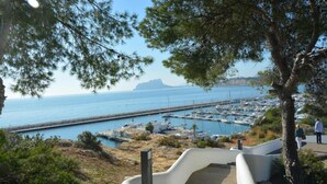 A coastal marina with boats docked, a clear sky, and a paved walkway leading to the water.