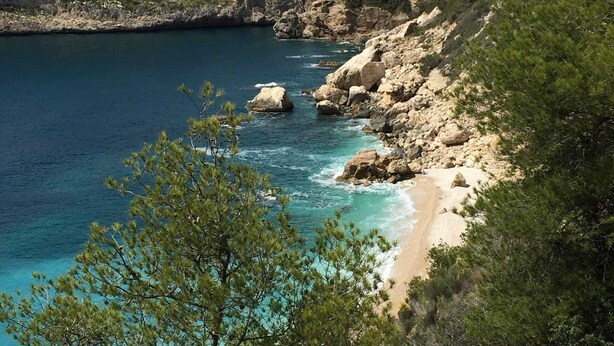 Paisaje costero con acantilados rocosos, aguas turquesas cristalinas y una playa de arena.