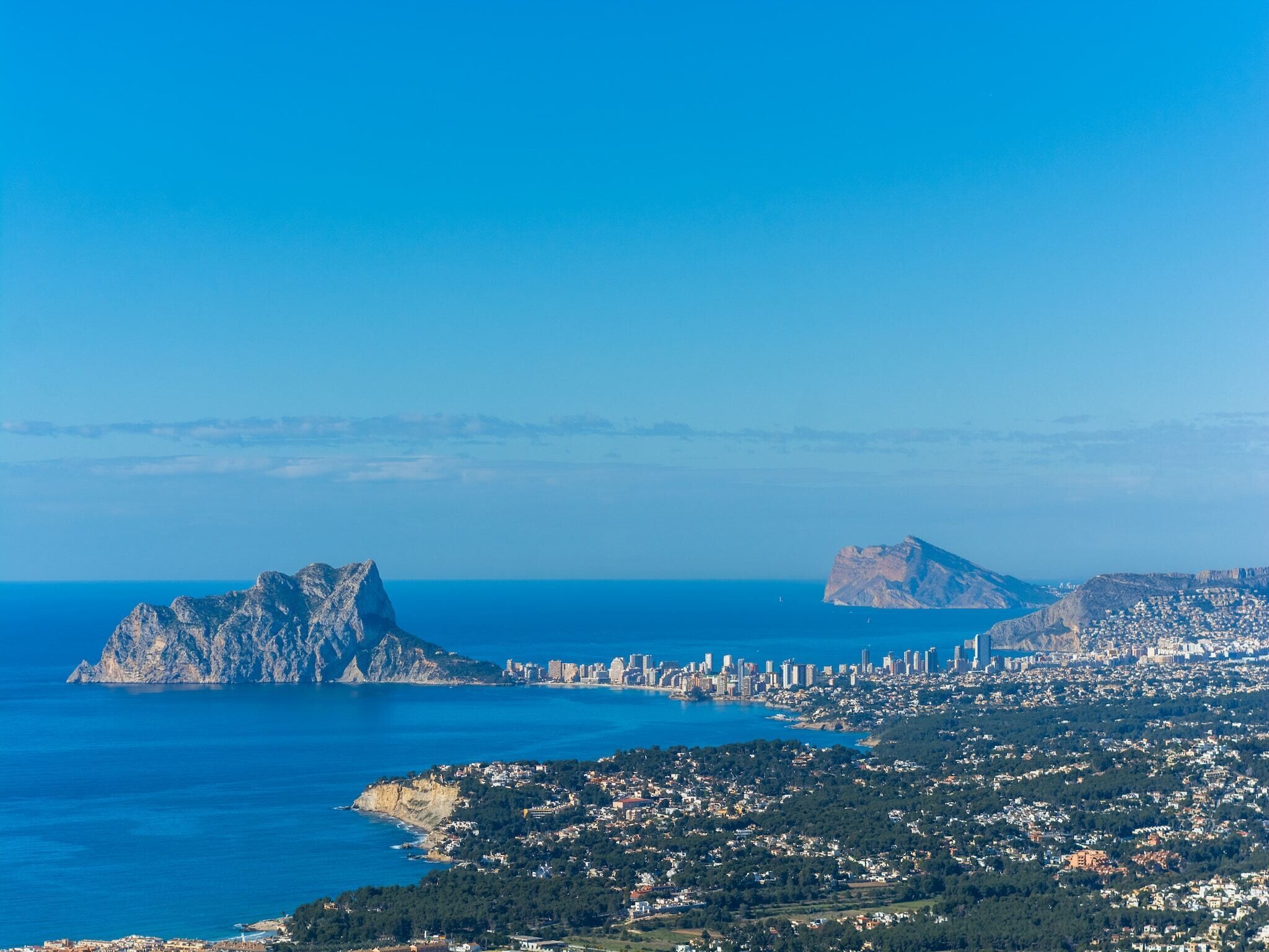 A coastal cityscape with a prominent rocky island and a dense urban area with buildings and greenery.