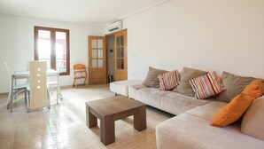 A living room with a sofa, a coffee table, a dining table with chairs, and a door.