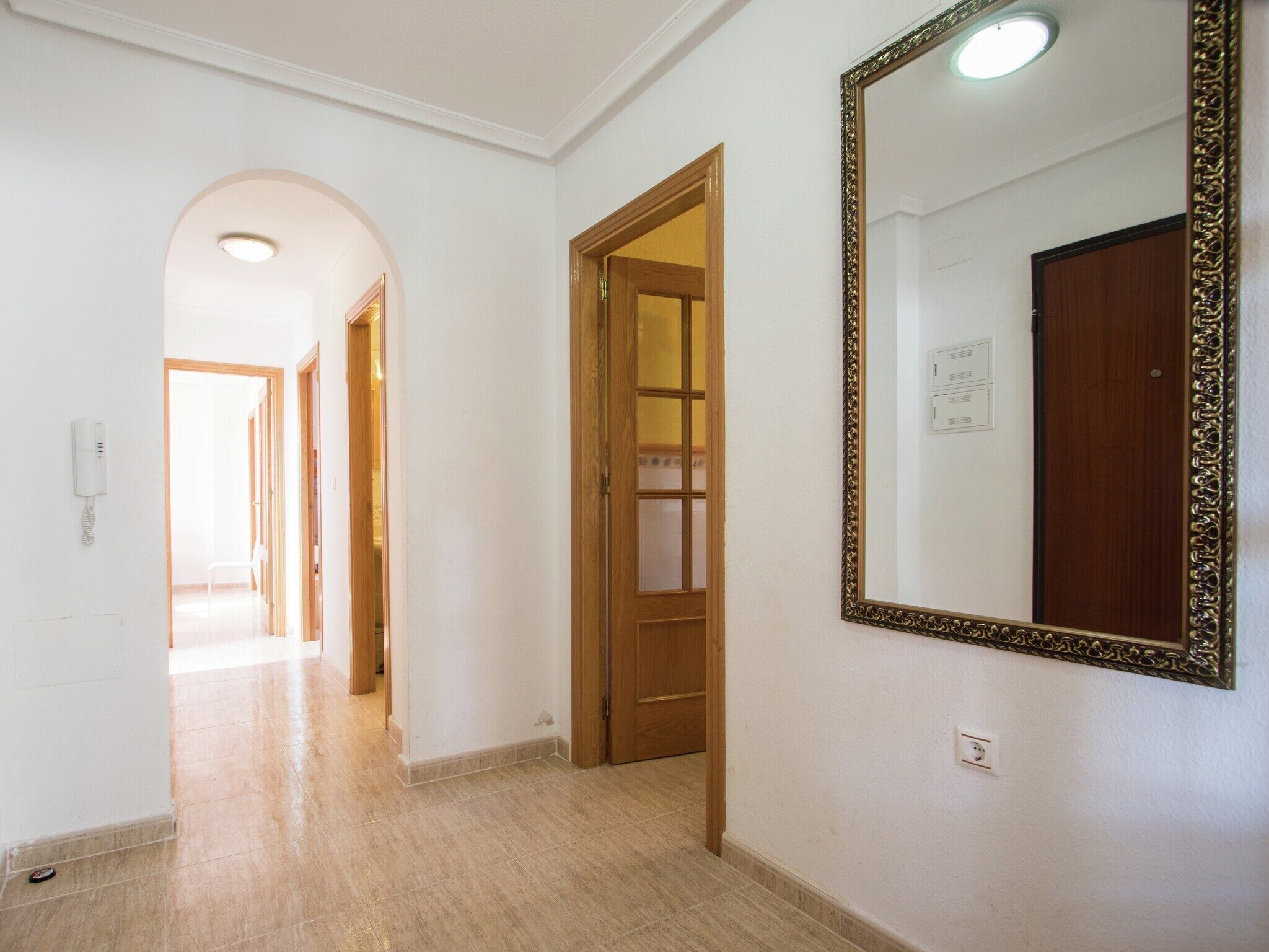 A hallway with a wooden door, a large mirror, and a phone on the wall.