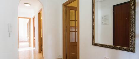 A hallway with a wooden door, a large mirror, and a phone on the wall.