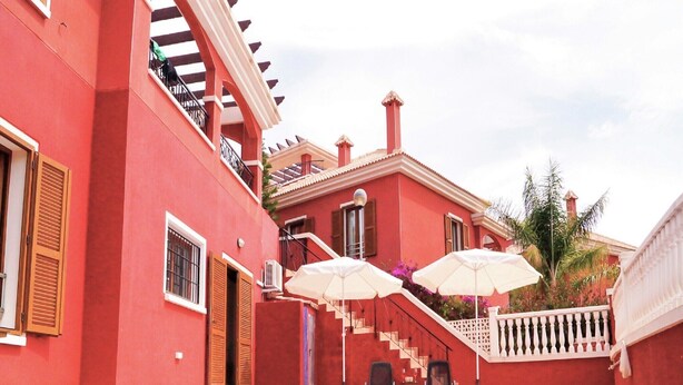 A red building with a pool, outdoor seating, and a staircase leading to a balcony.