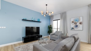 Un salon moderne doté d’un grand téléviseur à écran plat, d’un canapé gris, d’une table basse en verre et d’un mur d’accent bleu.