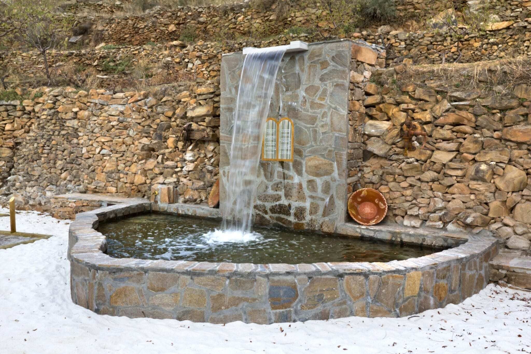 Een stenen waterpartij met een waterval, omgeven door een stenen muur en een met sneeuw bedekte grond.