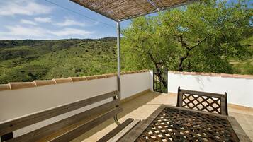 Un balcon doté d’un banc et d’une table en bois, offrant une vue sur un paysage verdoyant, avec des arbres et des collines.