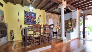 Un comedor con una mesa y sillas de madera, un tapiz colorido en la pared y un muro de piedra al fondo.