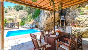 A covered outdoor area with a pool, wooden furniture, and a stone wall.