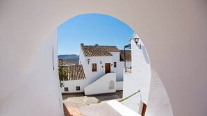 A narrow alleyway with white buildings, a tiled roof, and a clear blue sky.