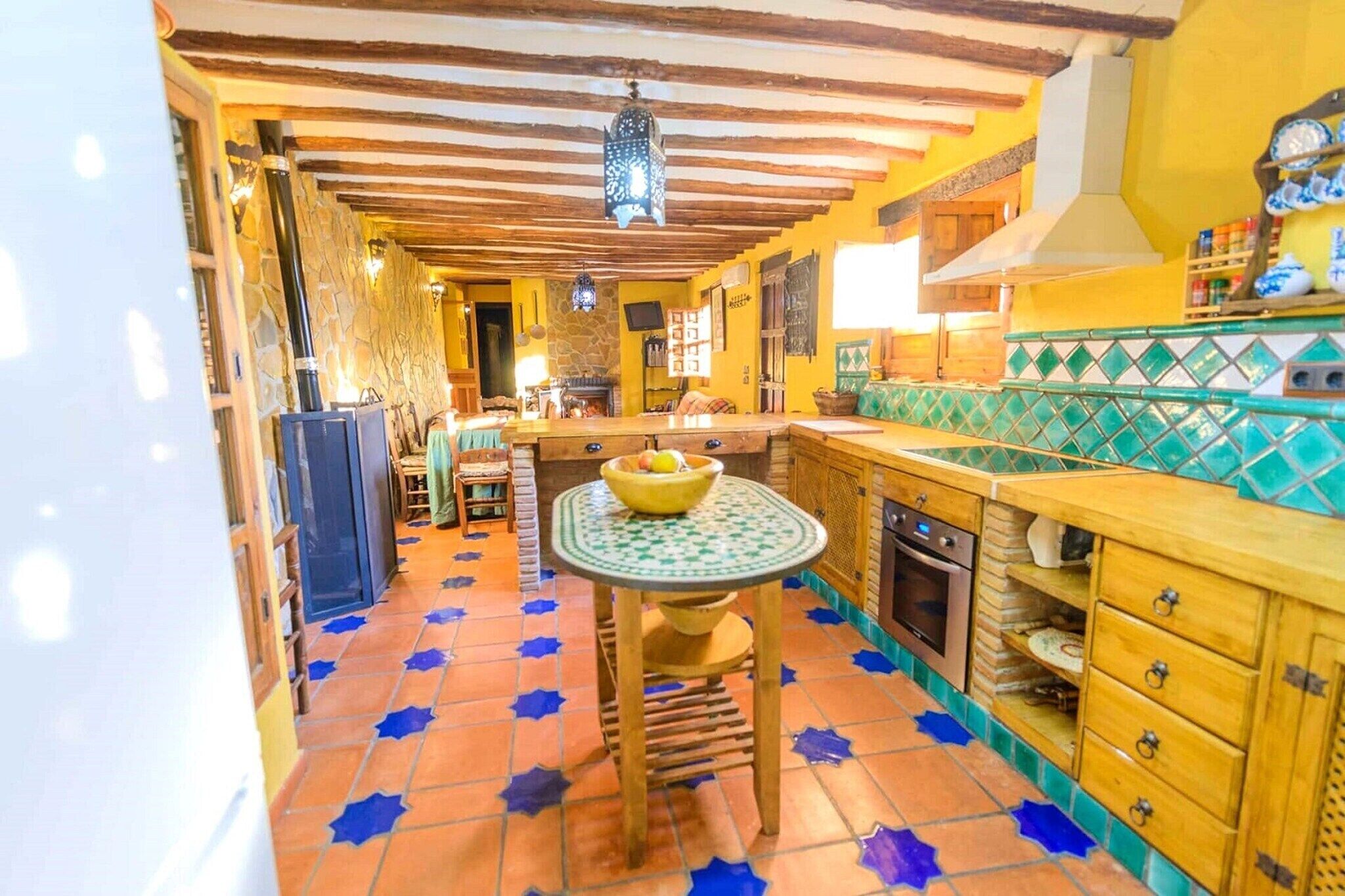 A kitchen with a tiled floor, wooden cabinets, a stove, and a dining area with a table and chairs.
