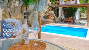 A poolside setting with a bottle of Lolea Beauty wine, two glasses, and a wicker table.