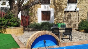 Un edificio de piedra con piscina, mobiliario exterior y un árbol.