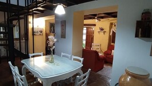Un comedor con una mesa, sillas, un jarrón con flores, un sofá rojo y una maceta grande.
