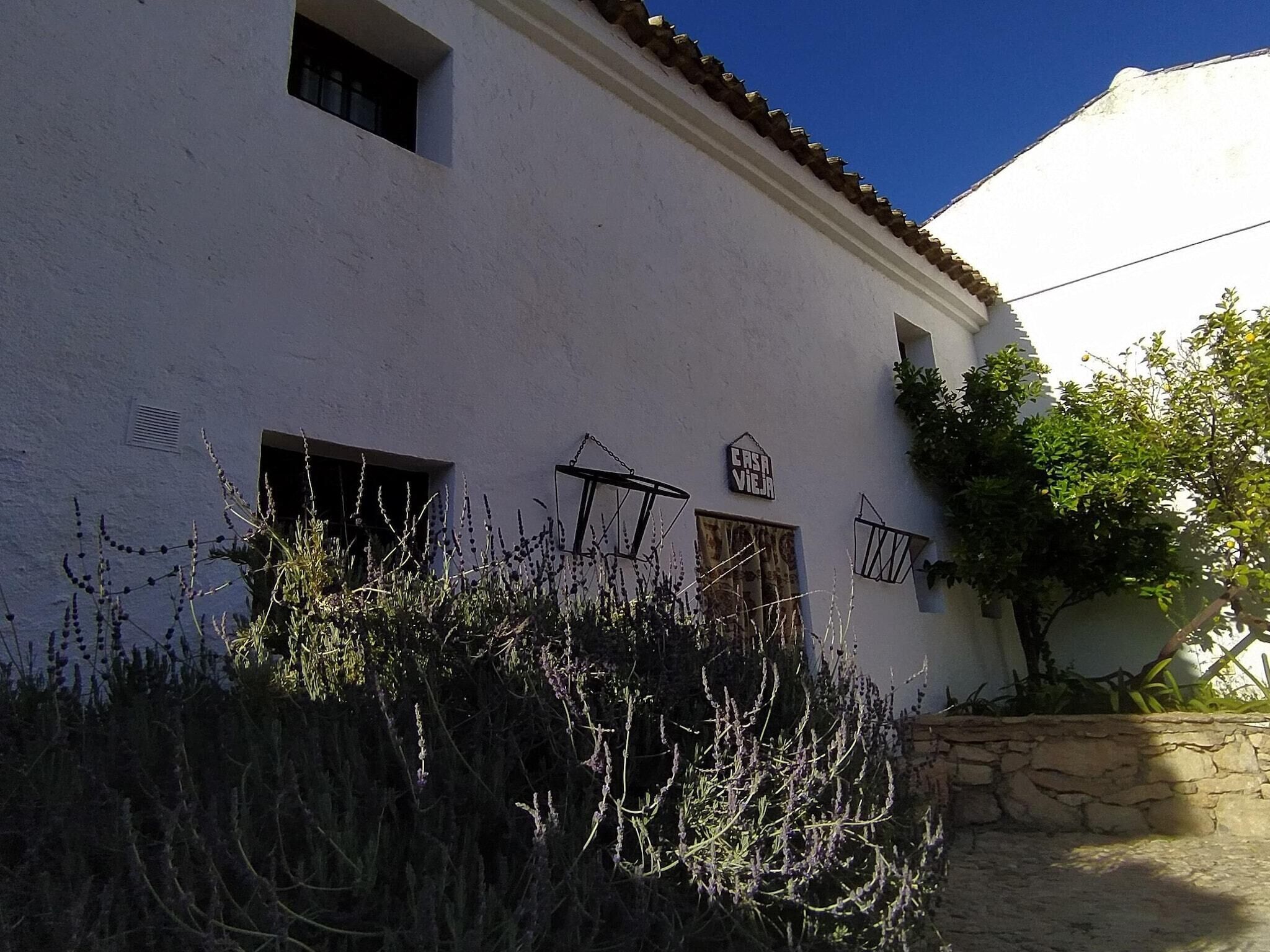 Un bâtiment blanc avec un mur en pierre, une fenêtre ornée d’une grille métallique et une enseigne sur laquelle on peut lire « CASA VIEIRA ».