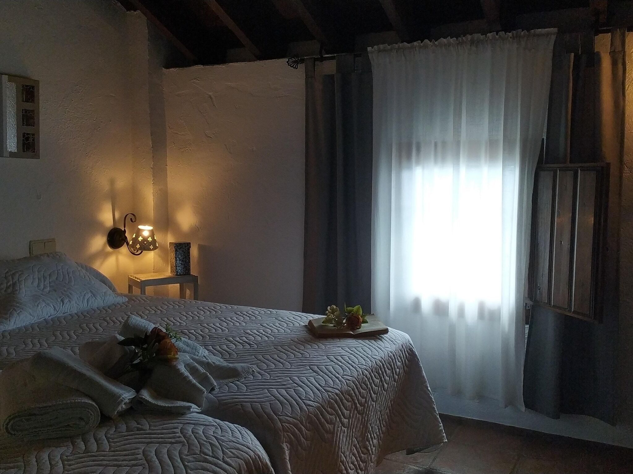 Ein Schlafzimmer mit einem Bett, einem Nachttisch, einer Lampe und einem Fenster mit Vorhängen.