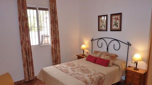 A bedroom with a bed, two bedside tables, a window with curtains, and two framed pictures on the wall.