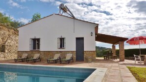 A poolside area with a white building, stone walls, and a clear blue pool.