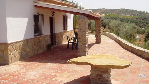 A patio area with a stone table, two chairs, and a white building with stone accents.