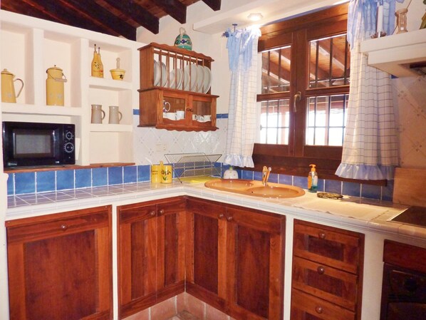 A kitchen with wooden cabinets, a microwave, a sink, and a window with curtains.