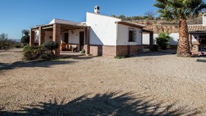 A single-story house with a covered porch, a small attached garage, and a palm tree in the foreground. - Spacious Cottage with Pool (Villanueva de la Concepción)