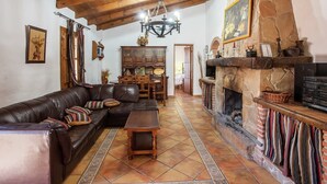 A cozy living room with a stone fireplace, wooden ceiling beams, and a leather sofa. - Spacious Cottage with Pool (Villanueva de la Concepción)
