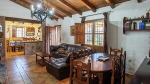 A cozy living area with a wooden ceiling, a stone fireplace, a leather sofa, and a dining table with chairs. - Spacious Cottage with Pool (Villanueva de la Concepción)